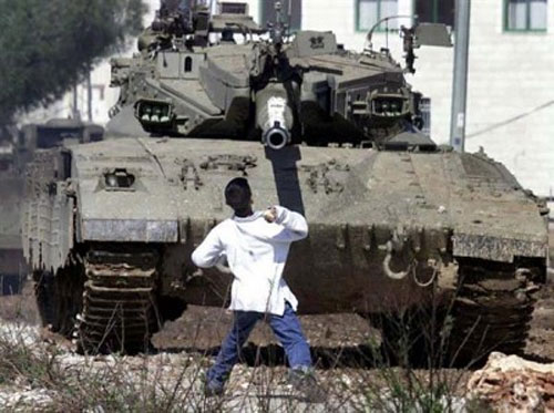 Le garçon Palestinien Faris Odeh (qui a ensuite été tué par les forces d’occupation) jette une pierre sur un blindé israélien pendant la 2e intifada (Source : flickr) 